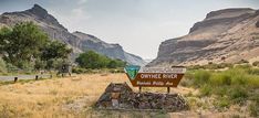 there is a sign in the middle of an open field with mountains in the background