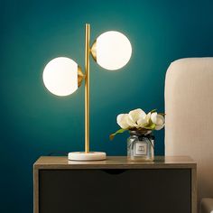 a table with a lamp on it next to a white chair and flower arrangement in a vase