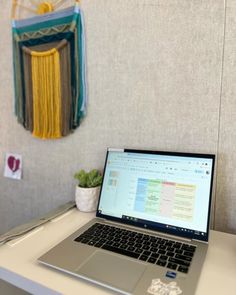 an open laptop computer sitting on top of a white desk next to a potted plant