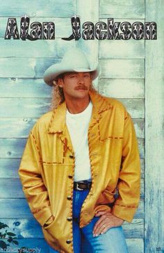 a man wearing a cowboy hat leaning against a wooden wall with his hands on his hips