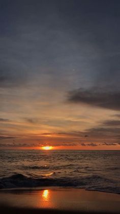 the sun is setting over the ocean with clouds in the sky and water on the beach