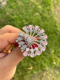 a person holding a pink and white brooch in their hand with grass behind it