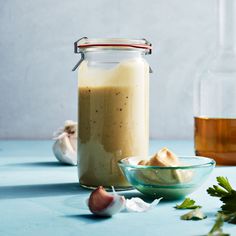 a glass jar filled with liquid next to garlic and an onion on a blue surface