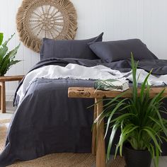 a bed with black linens and pillows in a white room next to a potted plant