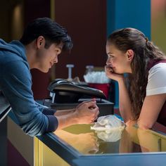 a man and woman sitting at a counter looking at each other