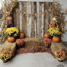 an arrangement of pumpkins, hay and flowers on display in front of a wooden fence