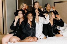 a group of women sitting on top of a bed in pajamas eating food and drinking