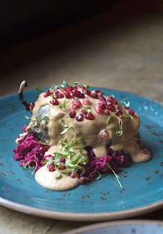 a blue plate topped with meat covered in sauce and garnished with pomegranates