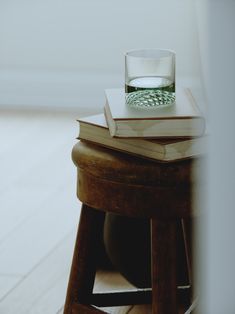 a stack of books sitting on top of a wooden stool next to a glass filled with water