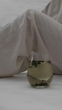 a glass filled with liquid sitting on top of a white sheet covered bed next to pillows