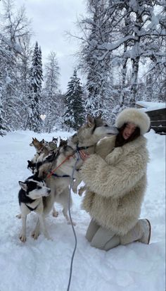 a woman is sitting in the snow with two dogs on leashes and she has her arms around her neck