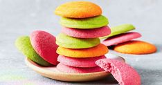 a pile of colorful cookies sitting on top of a wooden plate next to each other