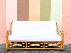 a wicker couch sitting in front of a wall with multicolored stripes on it