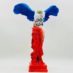 a statue with blue and red wings on it's head is in front of a white background