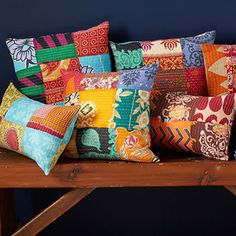 a bunch of colorful pillows sitting on top of a wooden bench in front of a blue wall