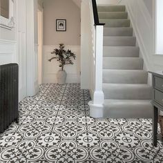 a white and black tiled floor in a hallway next to a stair case with a potted plant on it