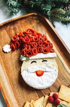 a wooden tray topped with crackers and cheese covered in santa claus's face