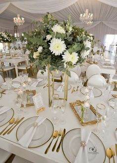 a table set up with white and gold plates, silverware and flowers in vases