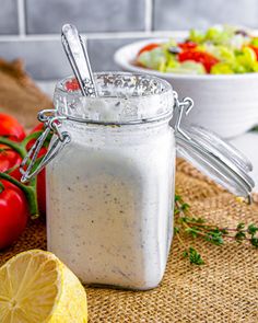 a glass jar filled with dressing next to a bowl of salad and lemon wedges