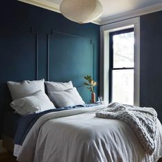 a bedroom with blue walls and white linens on the bed, along with a potted plant