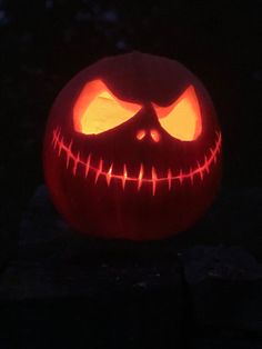 a carved jack o lantern in the dark with glowing eyes and fangs on it's face