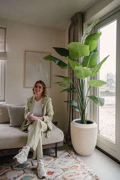 a woman sitting on a couch next to a potted plant in front of a window