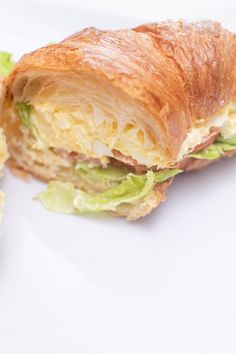 a croissant sandwich with lettuce and cheese on it sitting on a white plate