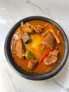 a bowl filled with meat and vegetables on top of a white countertop next to a red pepper