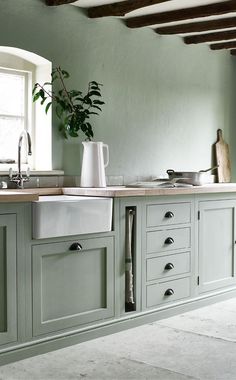 a kitchen with green cabinets and a white vase on the counter top, in front of a window