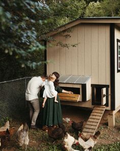 a man and woman kissing in front of a chicken coop with chickens around the house