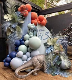 an elephant statue sitting on top of a wooden table next to balloons and palm trees