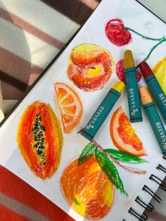 some crayons are sitting on top of a paper with fruit drawn on it