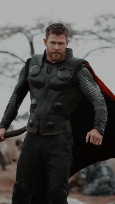 a man dressed as thor stands in the snow with his cape up and hands on his hips