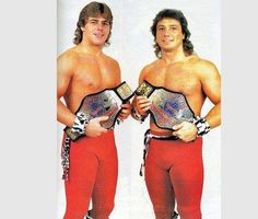 two men standing next to each other with wrestling belts in their hands and one wearing red pants