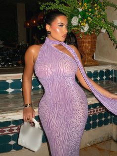 a woman in a purple dress is holding a white purse and posing for the camera