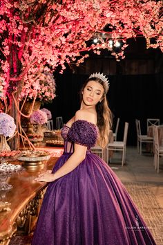 a woman in a purple dress standing next to a table with pink flowers on it