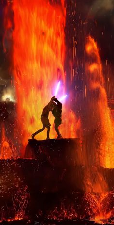 two people standing in front of a fire with bright orange and red flames behind them