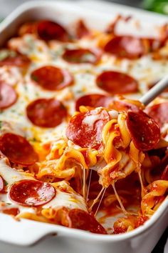 a white casserole dish with pepperoni and cheese on it, being lifted by a spatula