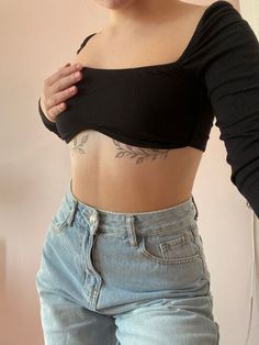 a woman with tattoos on her stomach wearing jeans and a black cropped top standing in front of a wall