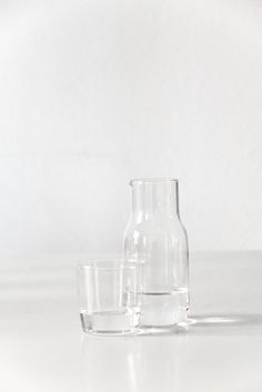 two clear glass vases sitting next to each other on a white surface with one filled with water