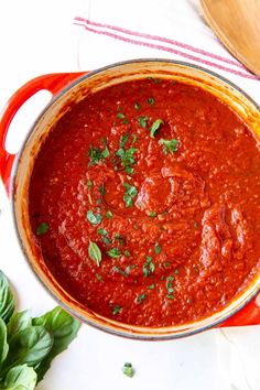 a red pot filled with sauce and garnished with parsley on the side