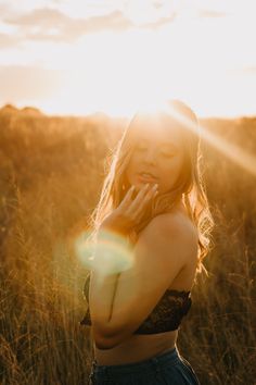 a woman standing in tall grass talking on a cell phone with the sun shining behind her