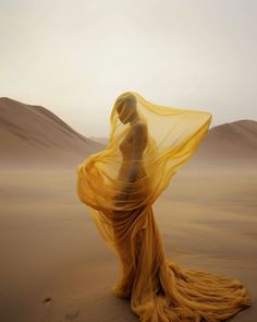 a woman is standing in the desert with her veil flowing over her head and body