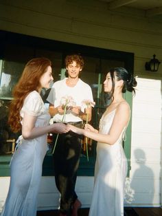 three young women standing in front of a house talking to each other while holding flowers