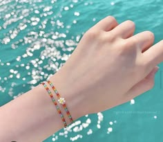 a woman's hand holding onto a bracelet with beads on it and water in the background