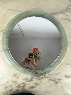 a person holding a camera in front of a round mirror on a marble counter top