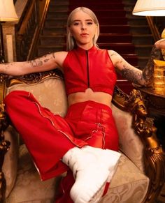 a woman sitting on top of a chair wearing red pants and a cropped top