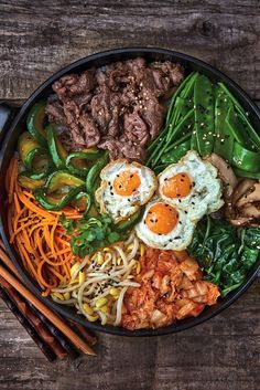 a bowl filled with meat and vegetables next to chopsticks on top of a wooden table