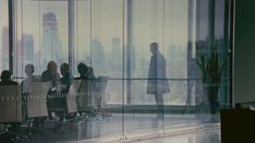 people are sitting at desks in an office with glass walls and floor to ceiling windows