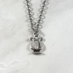 This beautiful chain necklace is the perfect way to express your affinity for Apollo or Ancient Greece. Made with a double sided Ancient Greek style lyre charm.  Secures with a lobster clasp. Chain is stainless steel and is available in a variety of lengths. (A two inch extender can be added to the end upon request.) Charm is made of pewter and is silver plated. Chain is stainless steel. All materials are lead and nickel free. Charm measures about 0.5 inches long. Pictured with a coin to give an Lyre Necklace, Apollo Necklace, Deity Altar, Greek Mythology Jewelry, Dragon Born, Mythology Jewelry, Altar Ideas, Silver Jewlery, Greek Style